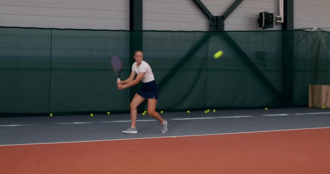 A tennis player hits balls at the back of the court, throws her racket after a failed serve. Two female tennis players play a training match on the court.
