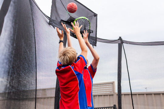 Happy siblings bouncing on trampoline playing ball game together after school