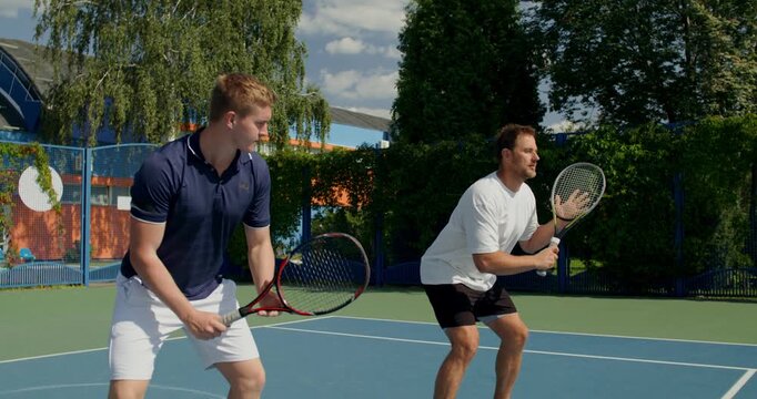 Close-up of two guys practicing their swing on the court. Two male tennis players train on the court with rackets in hand.