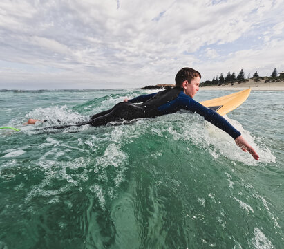 Youth Boy paddling fibreglass surfboard in ocean with urban coastal background