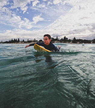 Youth Boy paddling fibreglass surfboard in ocean with urban coastal background