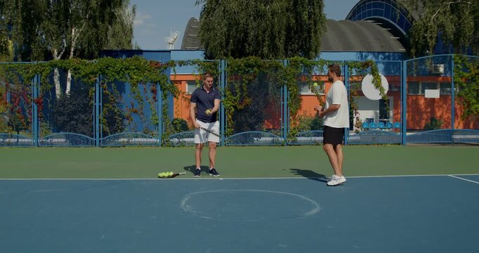 A guy serves with a tennis racket. Two male tennis players train on the court with rackets in hand.