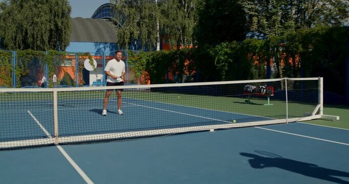 Guys practicing hitting the ball with a racket before the game. Two male tennis players train on the court with rackets in hand.