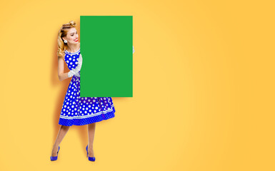 Beautiful woman in pinup blue dress pointing show board with free ad space. Full body pin up cute girl hold advertise offer promo, isolate yellow orange background. Spring season sale ad concept image