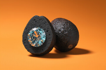Surreal conceptual image of a halved black avocado with a glowing teal center and a large sparkling diamond instead of a pit on an orange background.