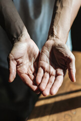  close-up view of two pairs of hands clasped together, suggesting a gesture of support, comfort, or connection. The hands appear to be intertwined, creating a sense of unity and togetherness. The back