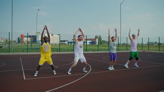 Basketball players perform jumps in place with arm swings during warm-up. Basketball players warm up before training.