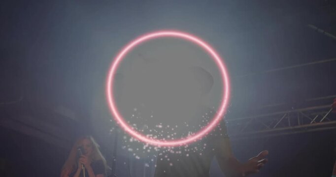 Male singer hitting high note causing pink neon ring swirling and backup singing on concert stage