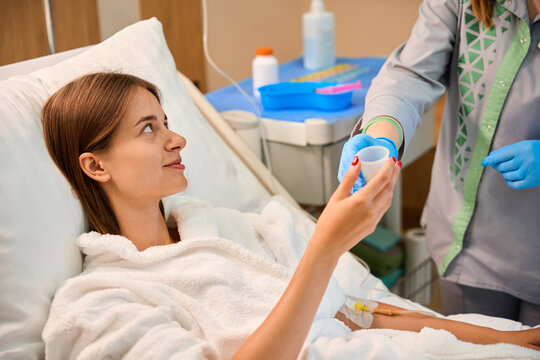 Woman lying in bed while nurse hands medication