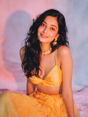 indian woman in yellow lehenga with long wavy hair and elegant jewelry posing on dreamy background