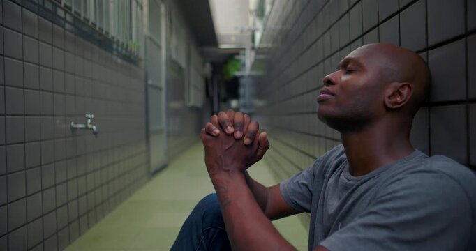 African American man sitting in narrow corridor with hands clasped in prayer, seeking guidance, hope during hardship, faith, quiet resilience, inner strength