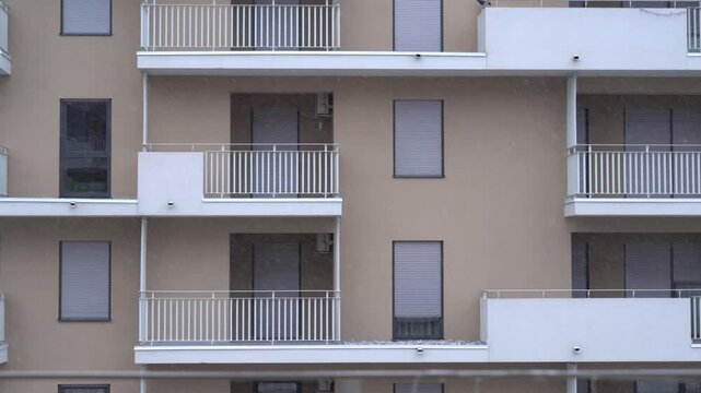 Static close-up shot of an apartment building facade with balconies during falling snow