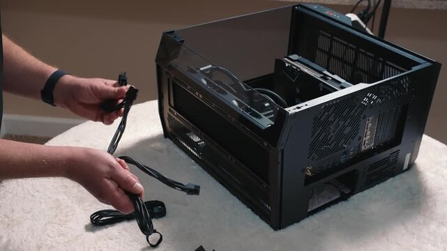 Selecting appropriate cables before connecting to motherboard, man holds two modular power supply cables in hands next to open computer case
