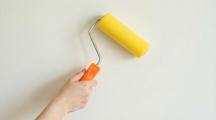 Hand holding yellow paint roller applying color to white wall