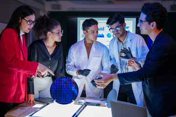 engineering research group analyzing a silicon wafer prototype. Professors and students collaborating on a microchip physics experiment in laboratory to develop future electronic technology.