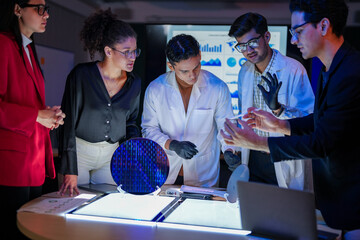 engineering research group analyzing a silicon wafer prototype. Professors and students collaborating on a microchip physics experiment in laboratory to develop future electronic technology.