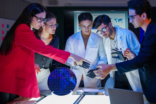 engineering research group analyzing a silicon wafer prototype. Professors and students collaborating on a microchip physics experiment in laboratory to develop future electronic technology.