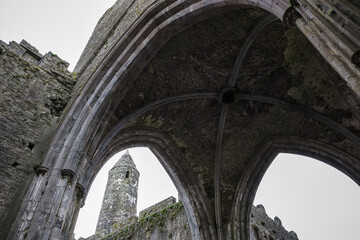 A upward view from the Rock of Cashel revealing weathered Gothic stone arches framing the round tower and ruins in County Tipperary, Ireland
