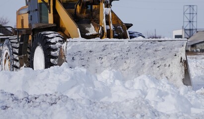 Close-up of a wheel loader bucket pushing snow in winter. Heavy construction machinery detail during snow removal and road maintenance in cold weather.