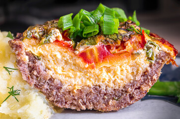 Fresh baked meat with cheese and tomatoes topped with chopped green onions and mashed potatoes next to it as a side dish