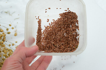 Flax seeds in a food-grade plastic container. Hand with flax seeds on a snowy background. Eating flax seeds in winter.