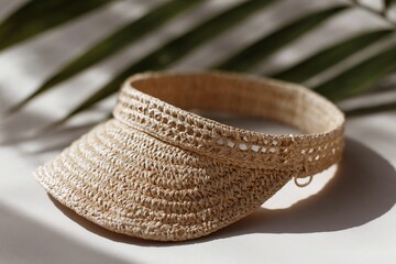 Woven straw visor hat with leaf shadows on neutral background
