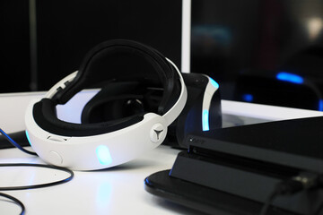 Virtual reality headset with sleek design and glowing accents placed on a modern workspace alongside a gaming console, showcasing advanced technology and immersive experiences