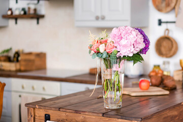 Bright kitchen interior featuring a beautiful floral arrangement in a glass vase on a wooden table, showcasing a warm and inviting atmosphere for home cooking and gatherings