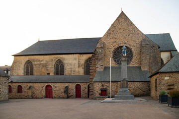 The facade of Notre Dame abbey in Paimpont, a village inside Broceliande forest. Exterior building and statue with no people at sunset. Brittany, France.