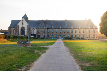 Entire view of Notre Dame abbey in Paimpont, a village inside Broceliande forest. Exterior building and pathway with no people at sunset. Brittany, France.