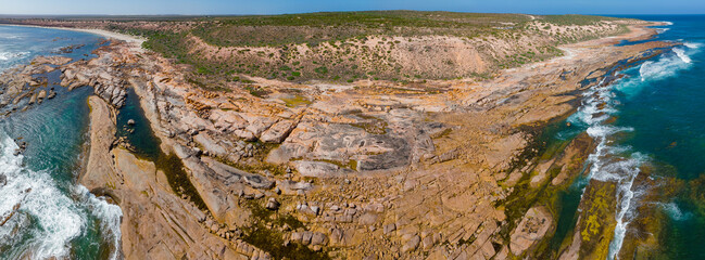 Aerial panorama view of a wide coastal rock ledge below a rugged plateau with ocean all around