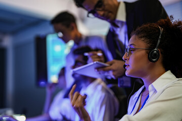 Professional financial trading team analyzing stock market trends in a modern office. Brokers with headsets discuss global investment strategies on a digital tablet at night.