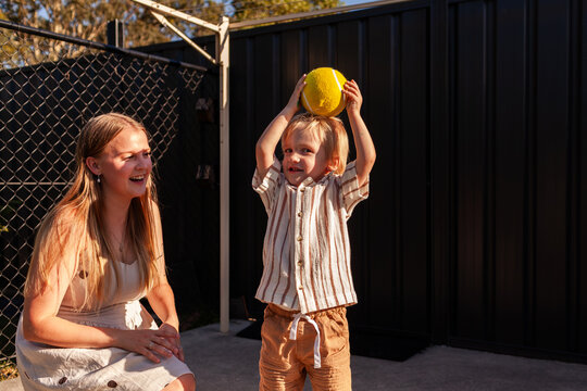 Young boy and mother playing in suburban backyard with yellow ball on summer afternoon