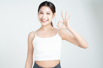 Beautiful young asian woman smiling with confident and OK finger pointing gesture and wearing a white top isolated on white background.