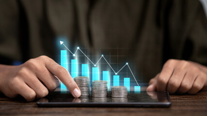 Businessman Touching Stacks of Coins on Tablet with Digital Financial Growth Graph