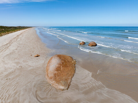 Aerial view of waves lapping against large granite boulders embedded in a sandy beach