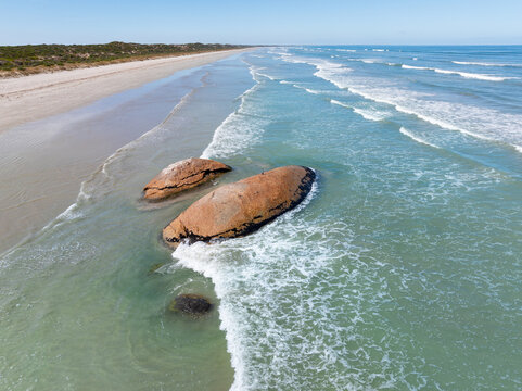 Aerial view of waves lapping against large granite boulders embedded in a sandy beach