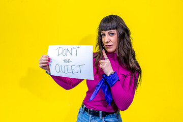 Woman showing don't be quiet sign and pointing finger on yellow background
