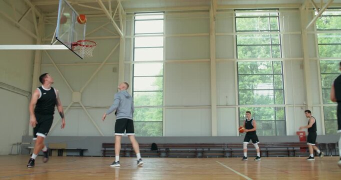 basketball coach explains the command how to brock the basket. a men's basketball team practices throwing the ball into the basket, the coach helps and suggests technique.