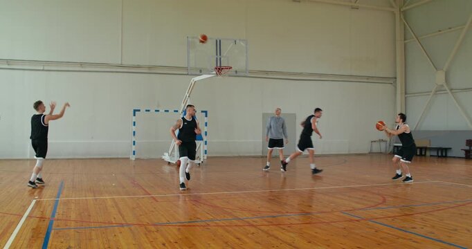 men practicing shooting. a men's basketball team practices throwing the ball into the basket, the coach helps and suggests technique.