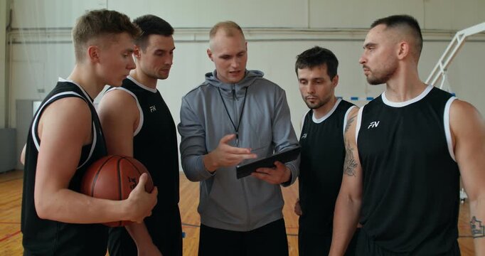 the coach is showing the tactics and game plan on the tablet. a coach and the team look at a tablet and discuss tactics for the upcoming game.