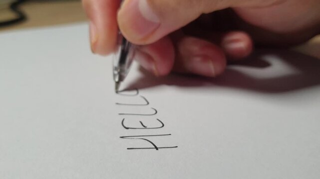 Close up footage of a hand writing the word Hello on white paper with a black pen, illustrating communication, greeting, welcoming concepts, and starting a letter.