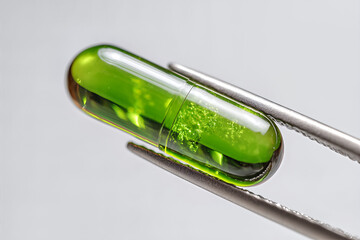 Macro close-up of a glossy translucent green capsule held by stainless tweezers — liquid gel supplement symbolizing modern pharmaceuticals and health
