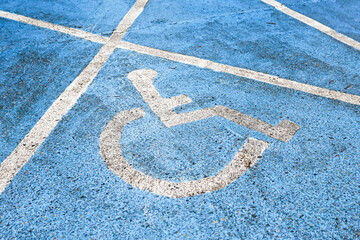 Disabled parking space symbol painted on blue asphalt. White wheelchair icon on reserved parking place. Accessibility sign on parking lot. Copy space for text or design. Dirty asphalt with paint.