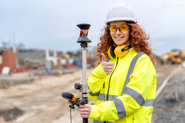 Young female surveyor operates a total station at a construction site while wearing safety hi-viz jacket