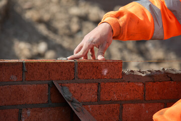 Bricklayer laying red bricks on construction site