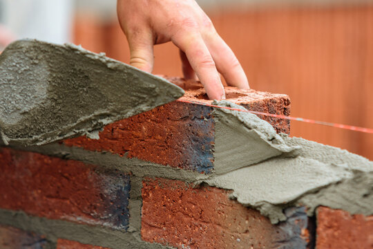 Close-up of builder laying red bricks for new structure wall at building site using tools and materials for masonry work