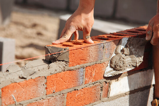 Close-up of Bricklayer constructing brick wall using red bricks, cement and tools