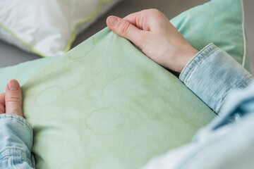 Female hands showing pillow in a living room. Dirty stains sweat or saliva on a green pillow. Conscious home care and sustainable living concept. top view