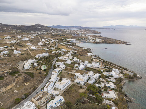 Aerial view of whitewashed buildings nestled along the rugged coastline where the azure sea meets the land, Paros, Paros, Greece.